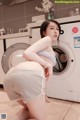 A woman in a white shirt and shorts is standing in front of a washing machine.