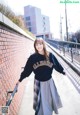 A woman leaning against a brick wall wearing a sweatshirt and skirt.