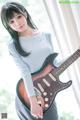 A woman holding a guitar in front of a window.