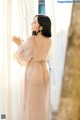 A woman in a pink dress standing by a window.