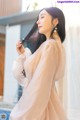 A woman in a beige dress standing by a window.