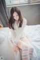 A woman sitting on top of a bed in a white shirt and striped socks.