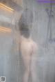 A naked woman standing in a shower next to a sink.