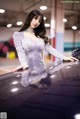 A woman in a silver dress leaning on a car.