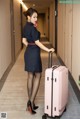 A woman in a blue dress holding a pink suitcase.