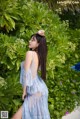 A woman in a blue dress standing in front of a bush.