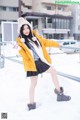 A woman in a yellow jacket and black skirt posing in the snow.