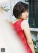 A woman in a red dress leaning against a wall.