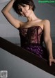 A woman in a purple corset leaning against a wall.