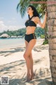 A woman in a black bikini standing next to a palm tree.