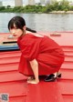 A woman in a red dress crouching down on a red boat.