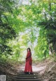 A woman in a red dress walking down a path in the woods.