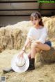 A woman sitting on a pile of hay wearing a cowboy hat.