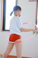 A woman in a white shirt and red shorts holding a hula hoop.