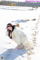 A woman in a white coat crouching down in the snow.