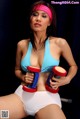 A woman in a blue top and white shorts holding two red and blue dumbbells.