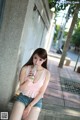 A woman sitting on the sidewalk drinking from a bottle.