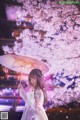 A woman in a white dress holding an umbrella under a tree.