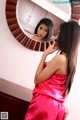 A woman in a pink dress looking at herself in the mirror.