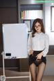 A woman in a white shirt and black skirt standing next to a white board.