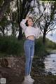 A woman in a white shirt and jeans standing by a river.