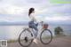 A woman riding a bike on a wooden boardwalk by the water.