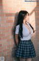 A woman in a school uniform leaning against a brick wall.