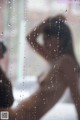 A woman standing in front of a window covered in rain.