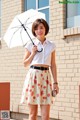 A woman standing in front of a brick building holding an umbrella.