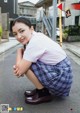 A young woman in a school uniform crouching down on the street.