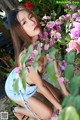 A woman in a blue dress crouching down next to a bush of flowers.