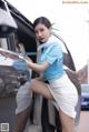 A woman in a blue shirt and white skirt leaning out of a car.