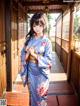 A woman in a blue kimono standing on a wooden walkway.