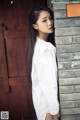 A woman leaning against a brick wall wearing a white shirt.