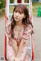 A woman sitting on a swing in a pink dress.