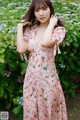 A woman in a pink dress standing in front of a bush.