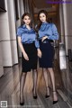 Two women in blue shirts and black skirts posing for a picture.