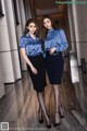 Two women in blue shirts and black skirts posing for a picture.