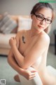 A naked asian woman with glasses sitting on a chair.