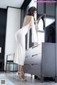 A woman in a white dress standing in front of a dresser.