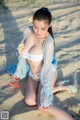 A woman in a white bikini sitting on a sandy beach.