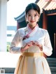 A woman in a white and gold hanbok holding a flower.