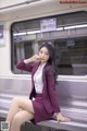 A woman in a purple suit sitting on a subway train.