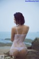 A woman in a white bodysuit sitting on a rock by the ocean.