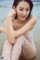 A woman in a white bodysuit sitting on the beach.