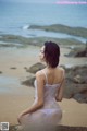 A woman in a white lingerie sitting on a rock by the ocean.