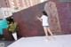 A woman in a white shirt and blue shorts spraying water on a wall.