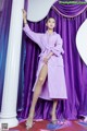 A woman in a purple robe posing in front of a purple curtain.