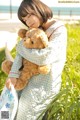 A woman holding a teddy bear in a field of tall grass.