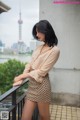 A woman standing on a balcony with a city in the background.